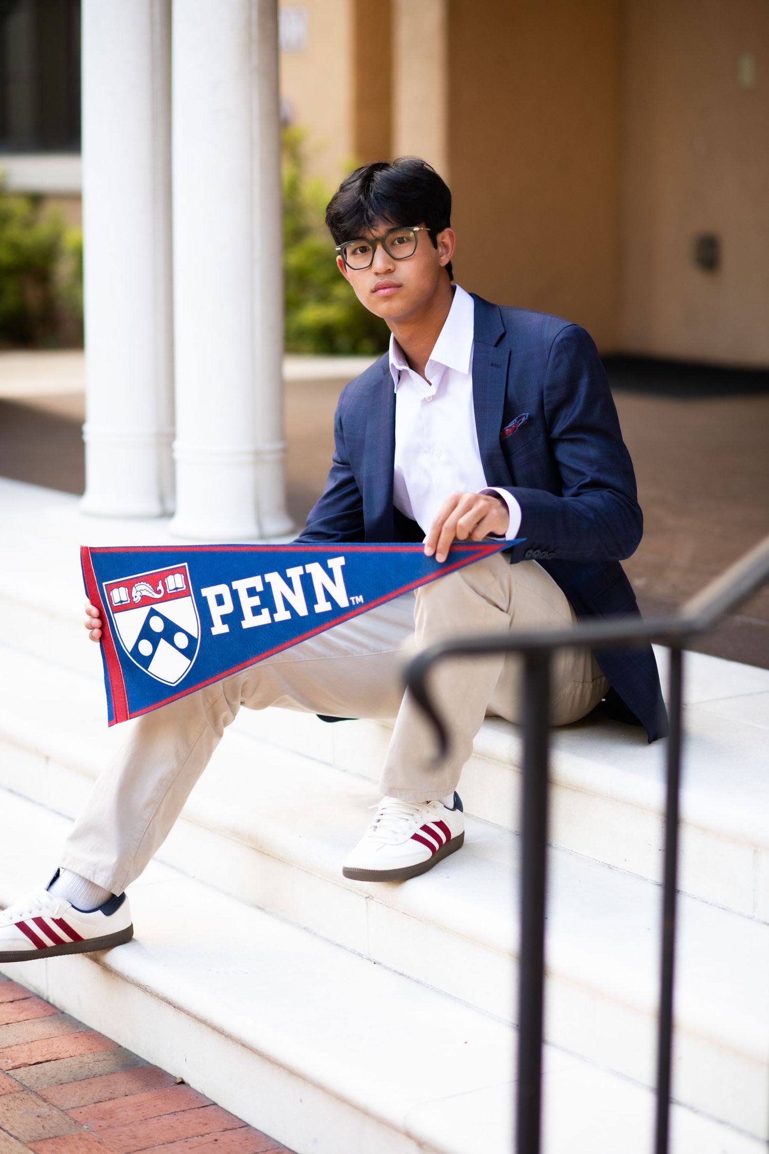 Young man in blazer holding a Penn University pennant flag while posing on white steps.