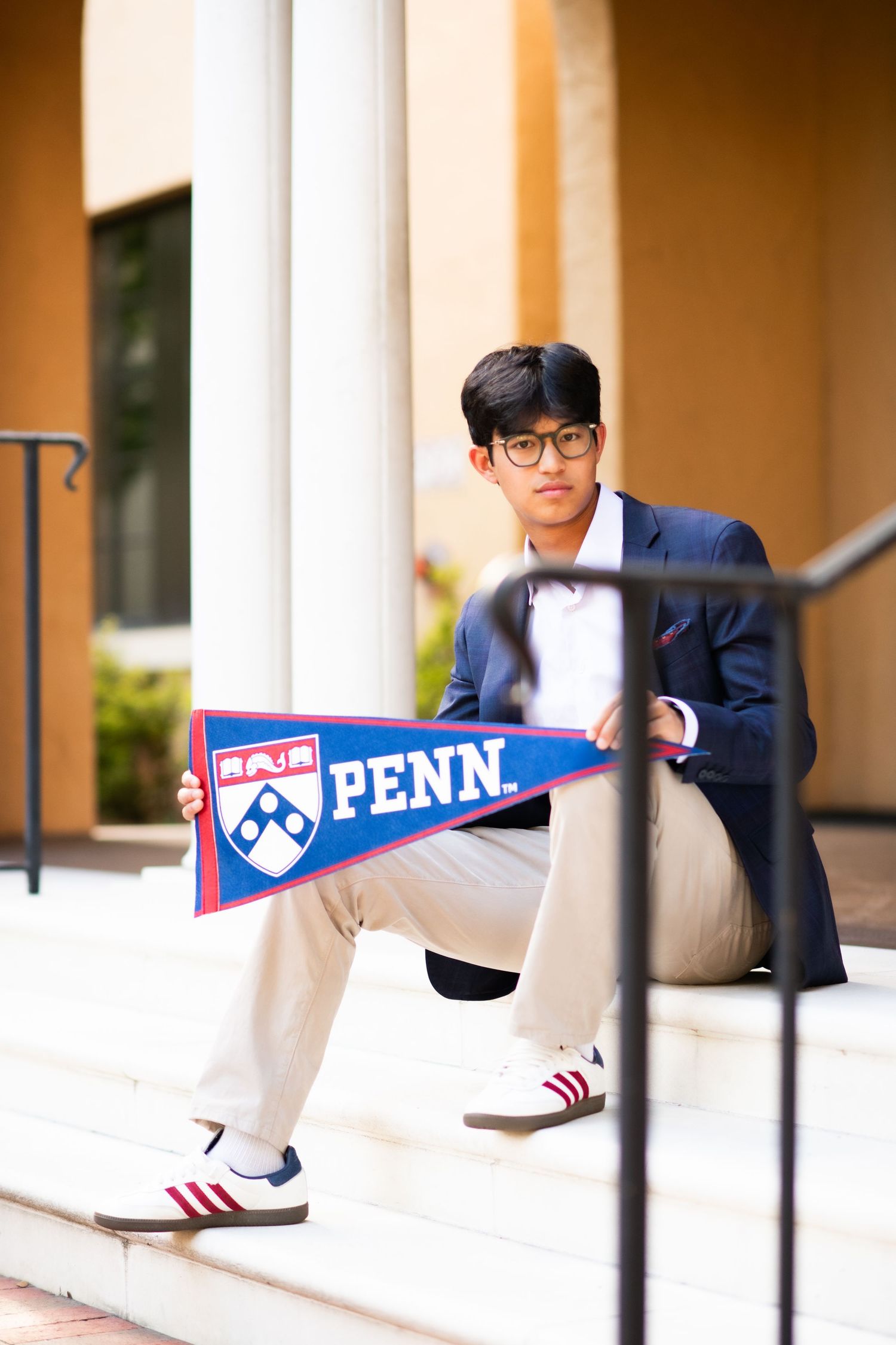 Young man in blazer crouching on steps holding a University of Pennsylvania pennant flag.
