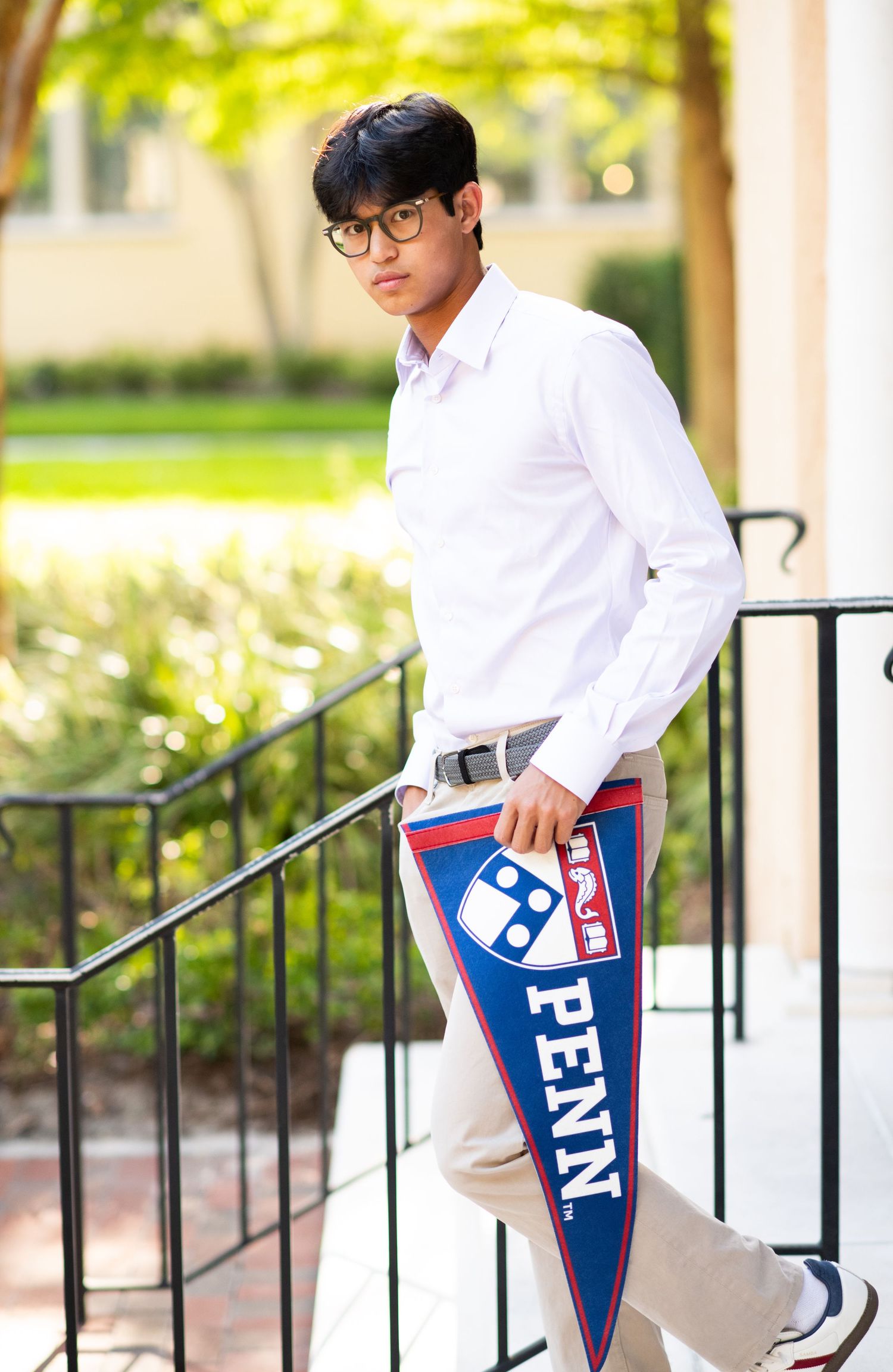 Teen boy in white dress shirt walking down steps holding a Penn university pennant.