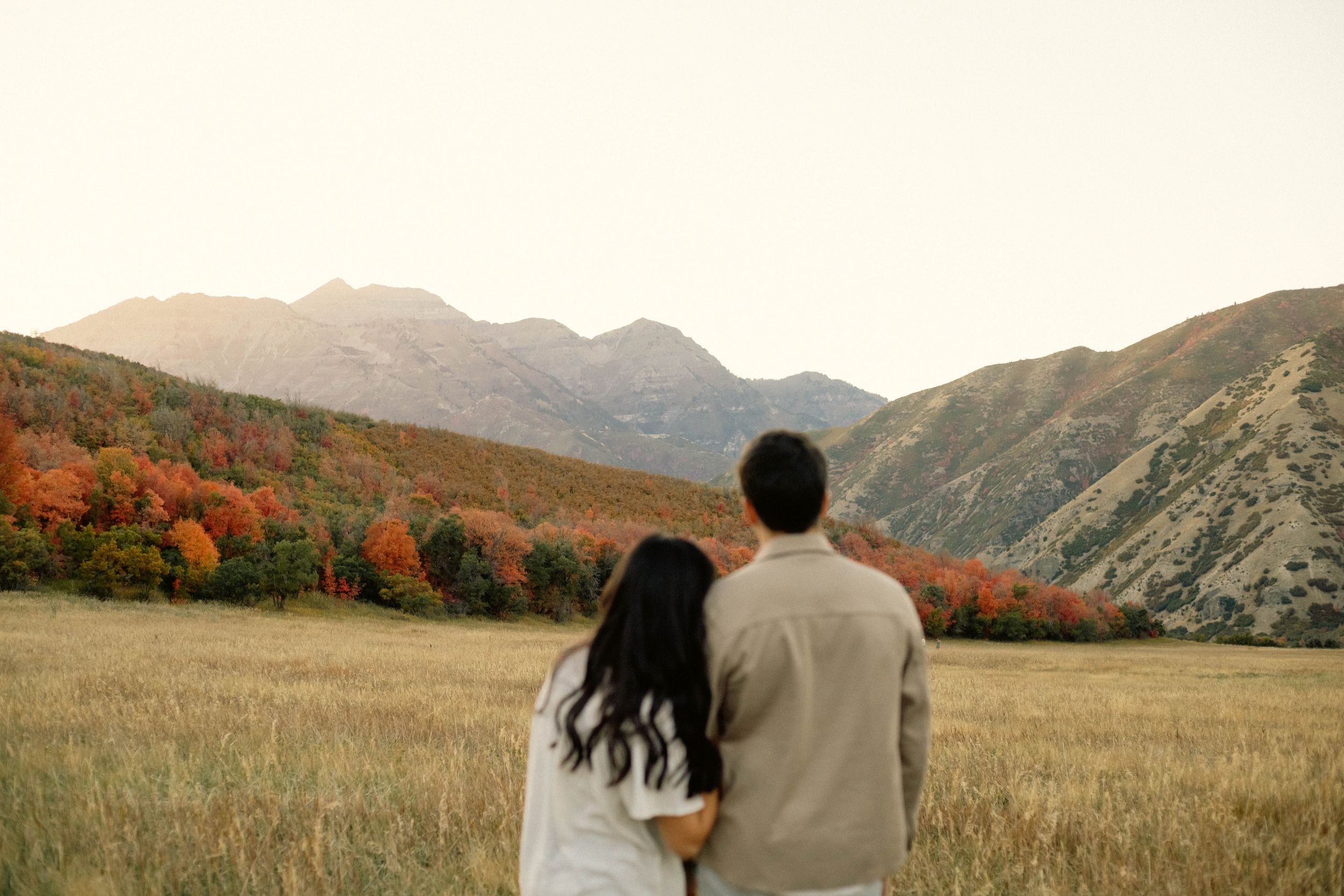 Couple embracing while admiring autumn mountain landscape with colorful fall foliage and golden fields at sunset.