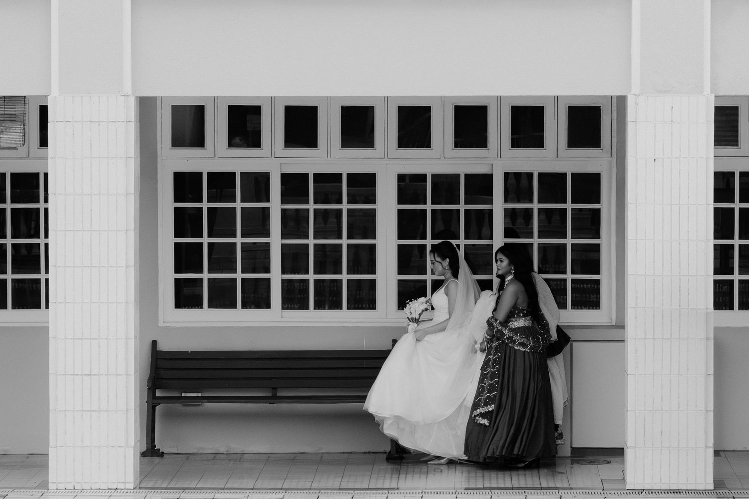 Muslim bride and groom celebrating wedding entrance with guests, bride in white hijab gown, indoor venue with white columns.