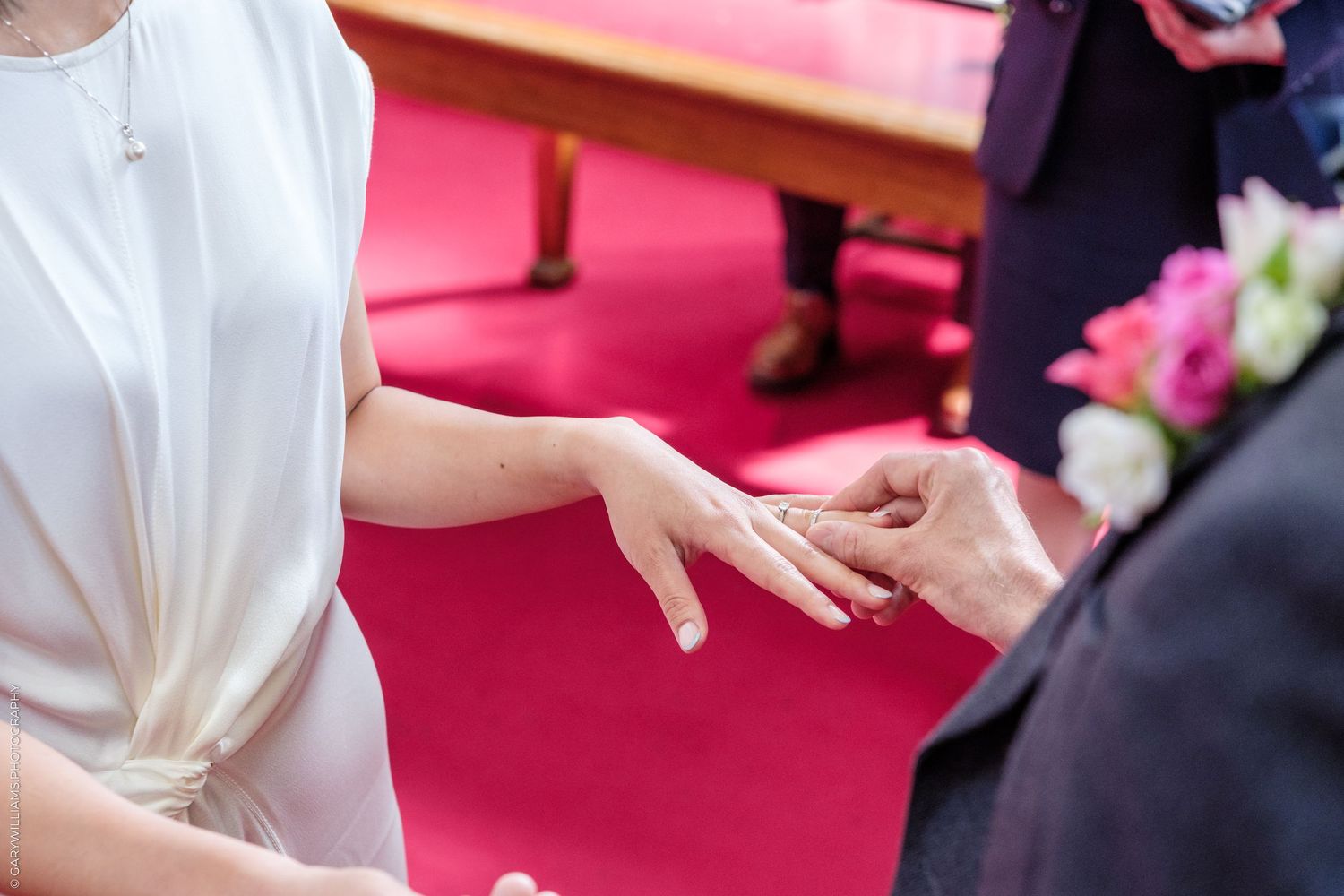 Close-up of wedding ring exchange ceremony, bride in white dress receiving ring from groom.