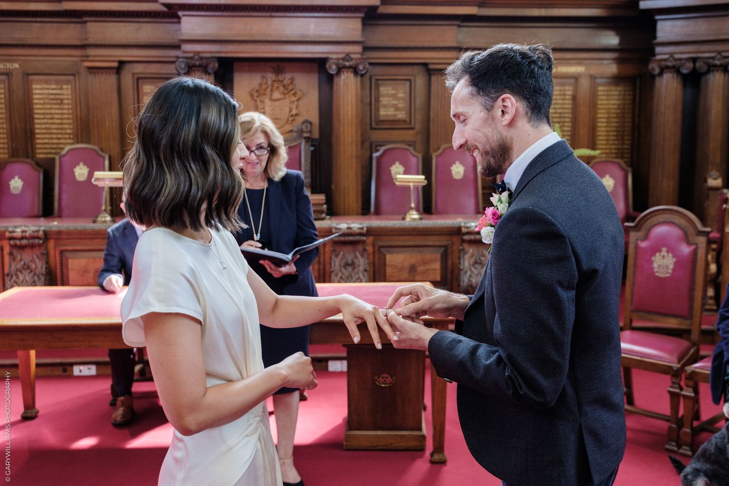 Couple exchanging rings during a civil wedding ceremony in an elegant wood-paneled room with an officiant.