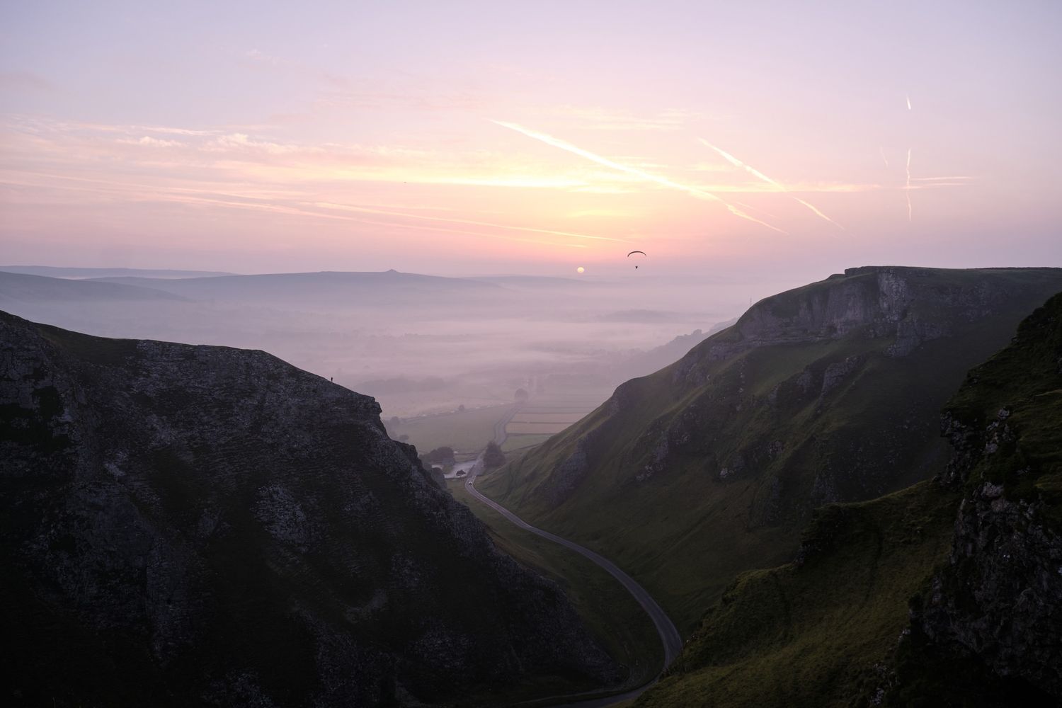 Stunning pink and purple sunrise over a misty valley between dramatic green cliffs and hills.