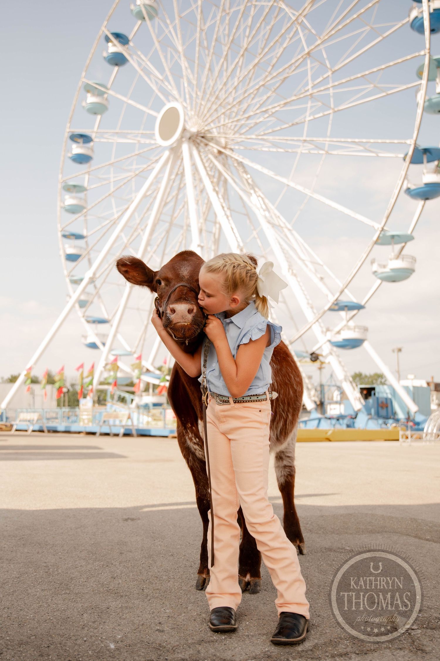 Young girl hugging a brown calf in front of a white Ferris wheel at a county fair.