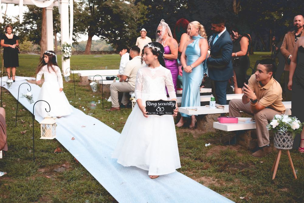 Flower girl walking down white aisle runner at outdoor wedding ceremony.