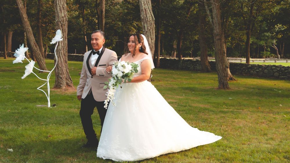 Bride in white ball gown and groom in tuxedo walking on green grass with decorative white doves at outdoor wedding.