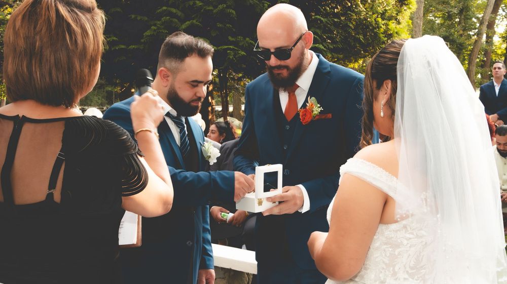 Groom presenting wedding ring box to bride at outdoor ceremony.