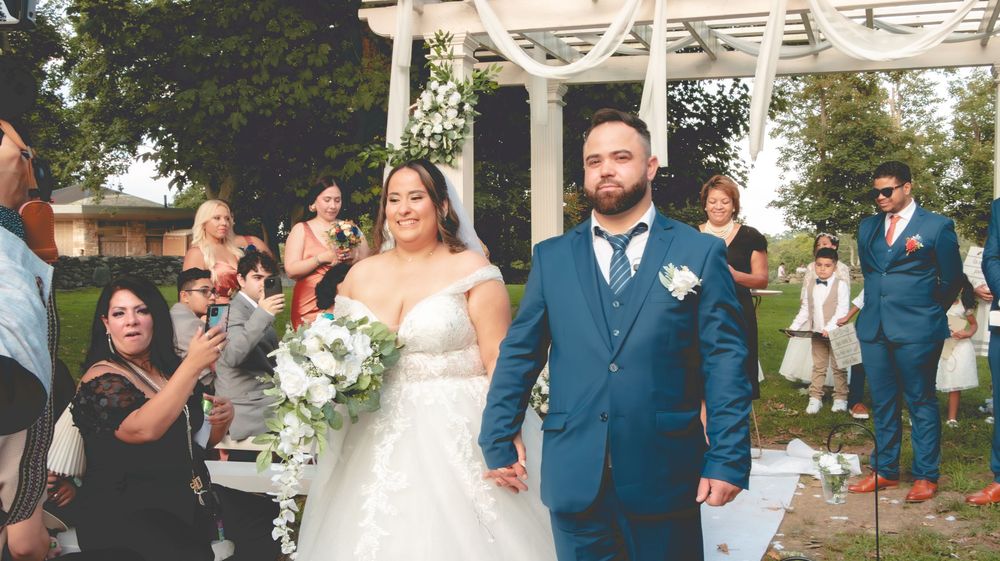 Newlywed couple walks down the aisle at an outdoor wedding ceremony surrounded by cheering guests.