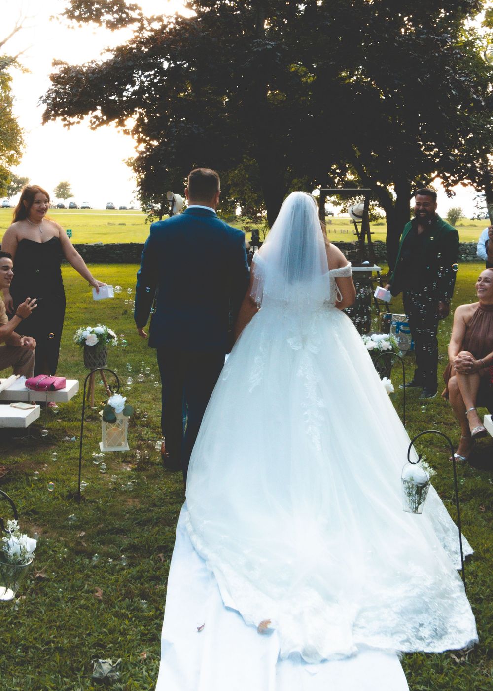 Bride and groom walking down outdoor wedding aisle surrounded by guests at golden hour.