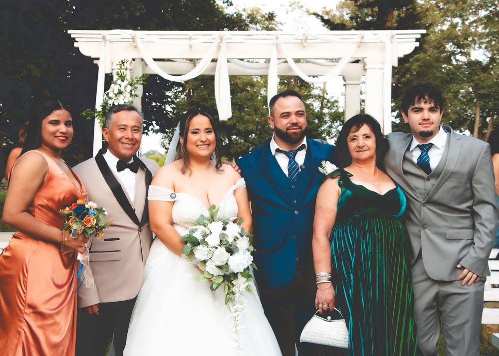 Bride and groom posing with family members in front of white wedding arch outdoors.