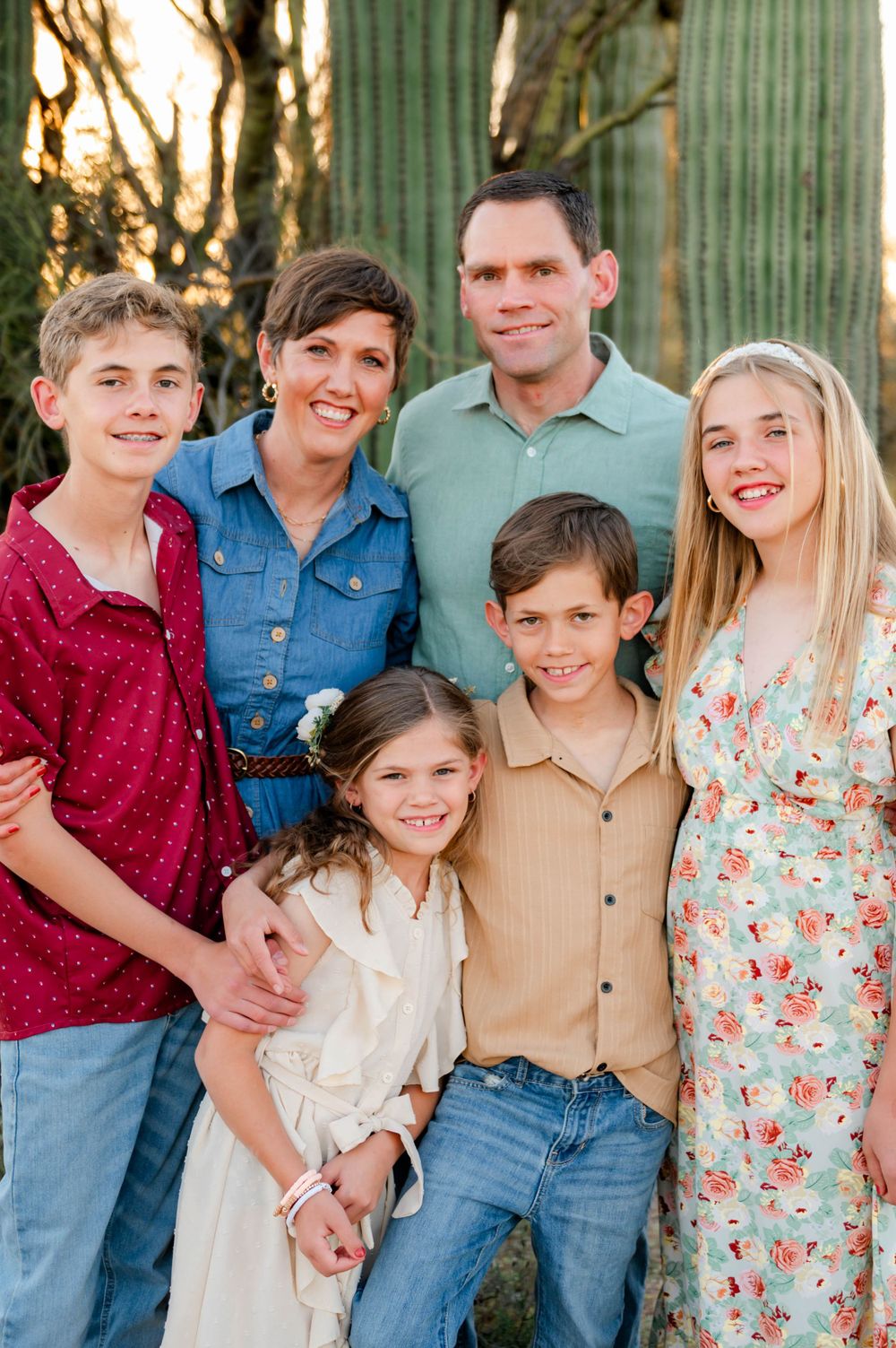 Family of six poses together smiling near saguaro cactus in warm desert sunset photography session.