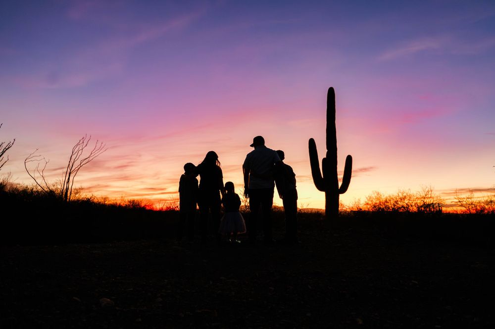 Silhouette of a family with a saguaro cactus against a vibrant Arizona desert sunset sky.