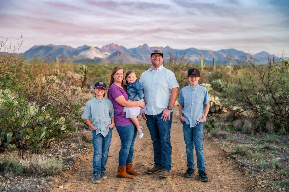 Family of five poses on a desert trail with mountain backdrop and saguaro cacti in Arizona.