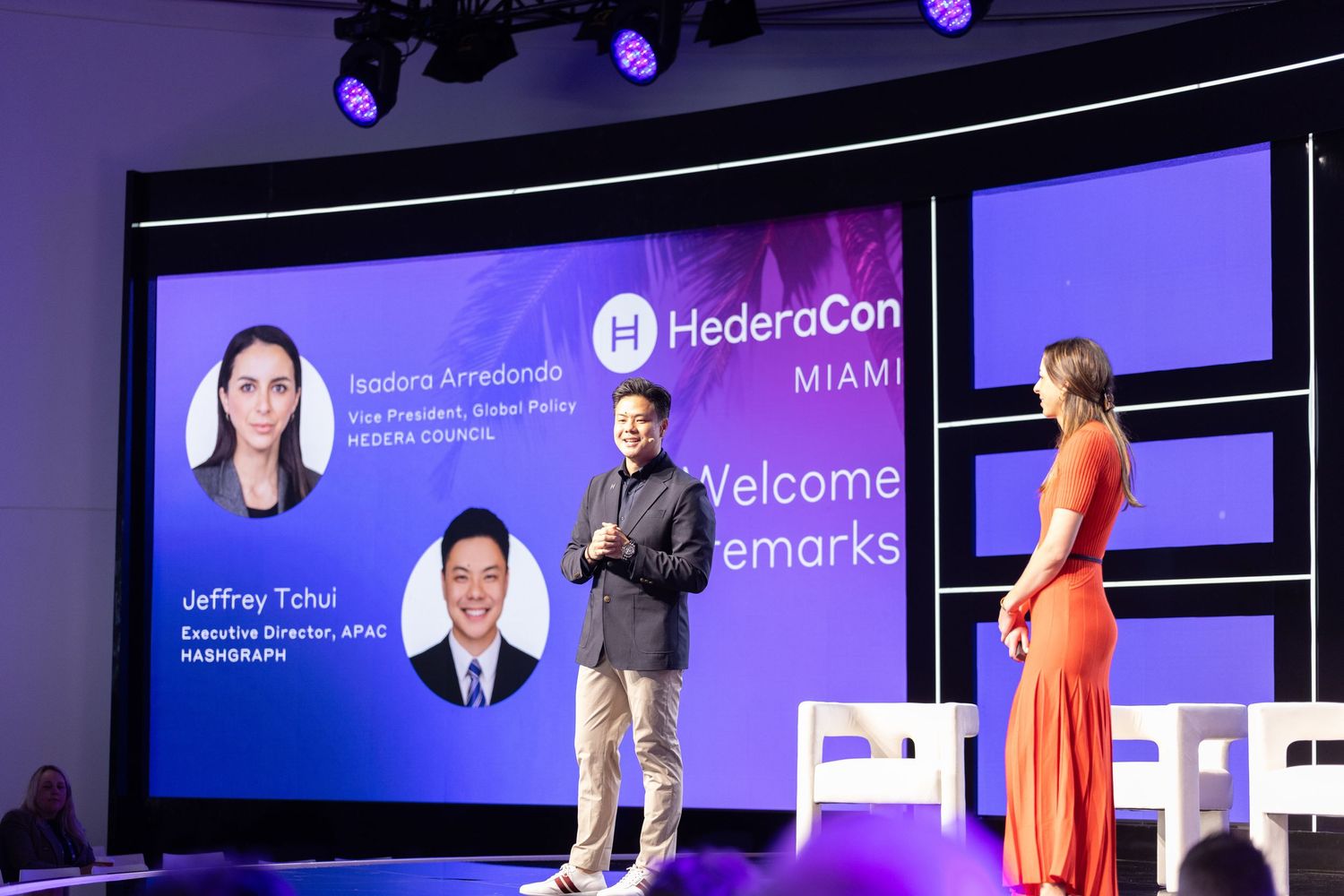 HederaCon Miami panel featuring Isadora Arredondo and Jeffrey Tchoi on stage with a presenter in an orange dress.