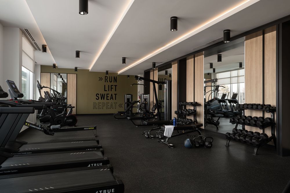 Modern gym with treadmills, free weights, mirrors, and motivational Run Lift Sweat Repeat wall sign.