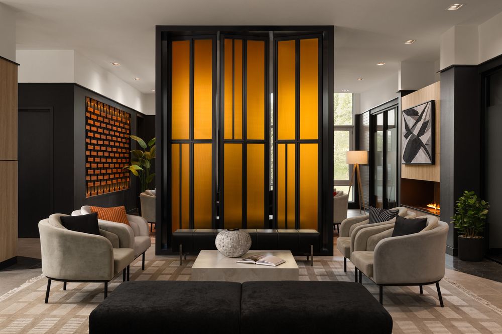 Modern hotel lobby with glowing amber partition, elegant gray armchairs, and sophisticated black and wood decor.