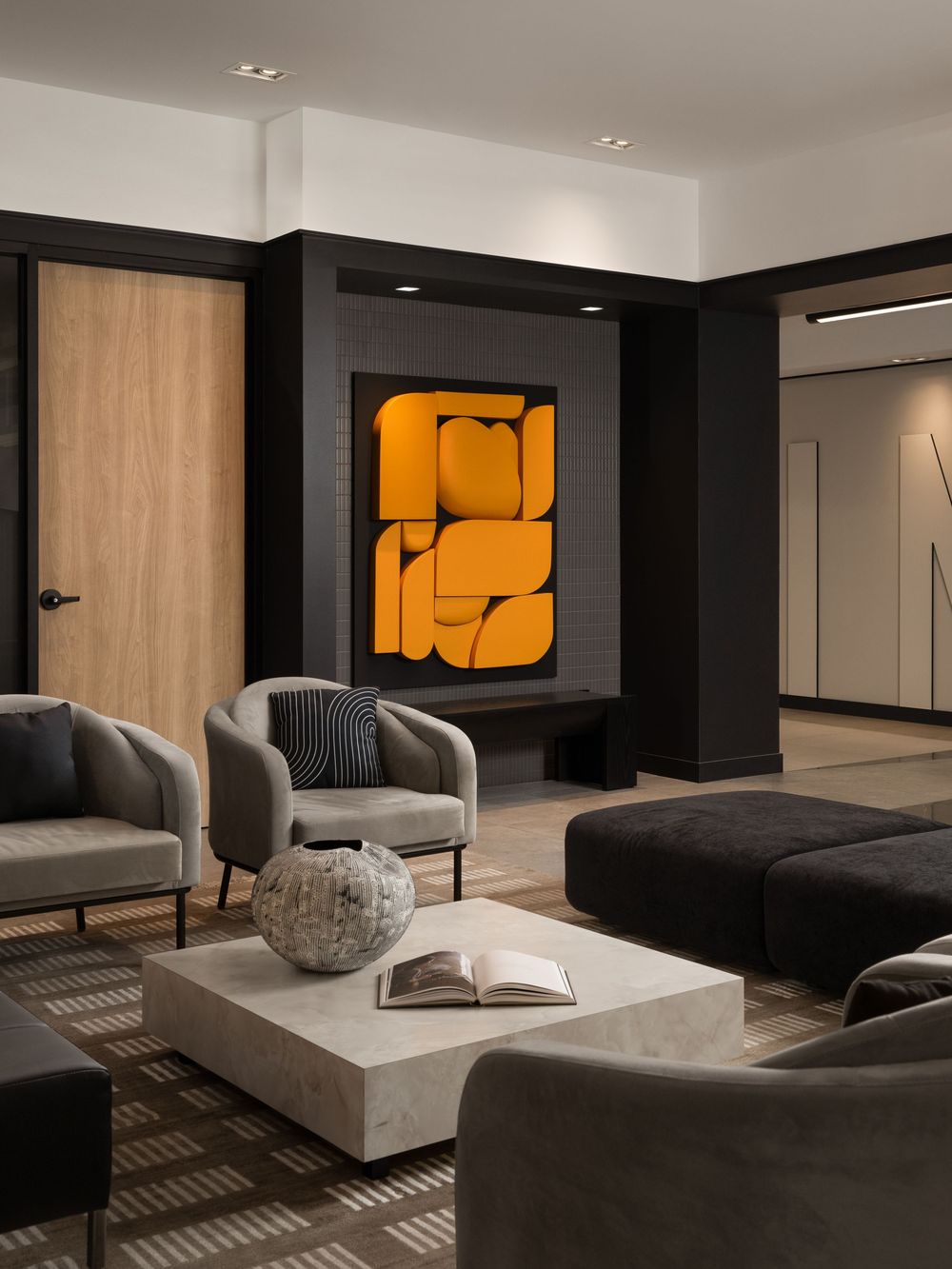 Modern living room with gray armchairs, marble coffee table, and bold orange abstract artwork above a dark fireplace.