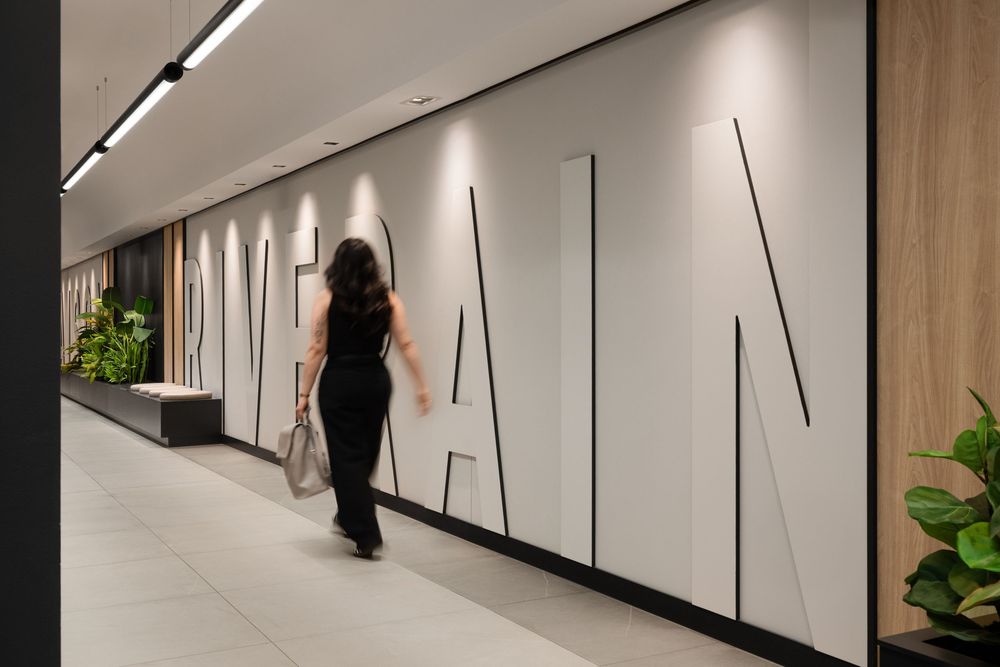 Woman walking through modern office corridor featuring large geometric typography wall art with sleek lighting.