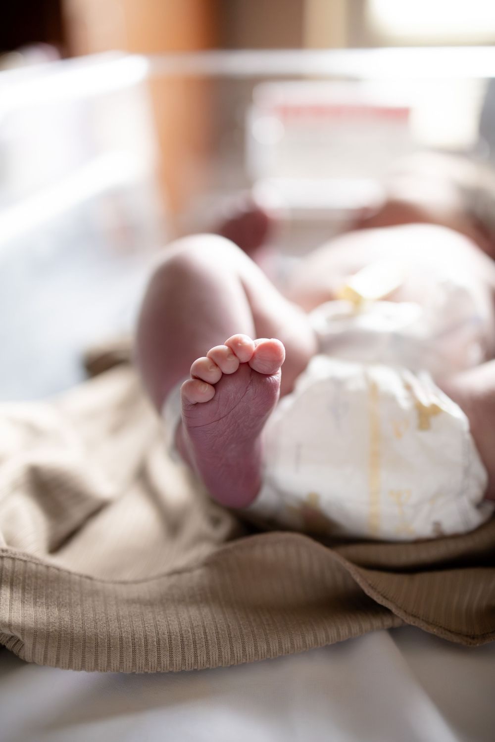 Close-up of tiny newborn baby feet resting on a soft blanket in a hospital bassinet.