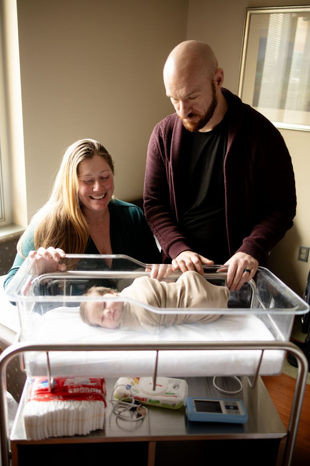 New parents smiling over their newborn baby in a hospital bassinet, celebrating the birth in a maternity ward.