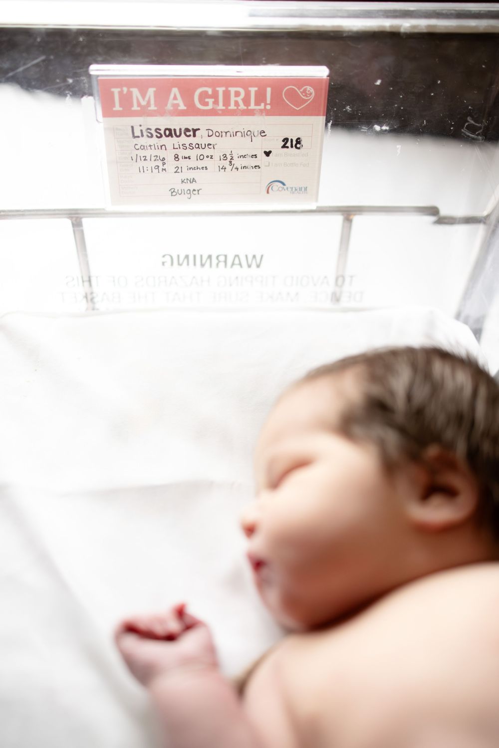 Newborn baby girl named Lissauer Dominique resting in hospital bassinet with pink I'm a Girl name card.