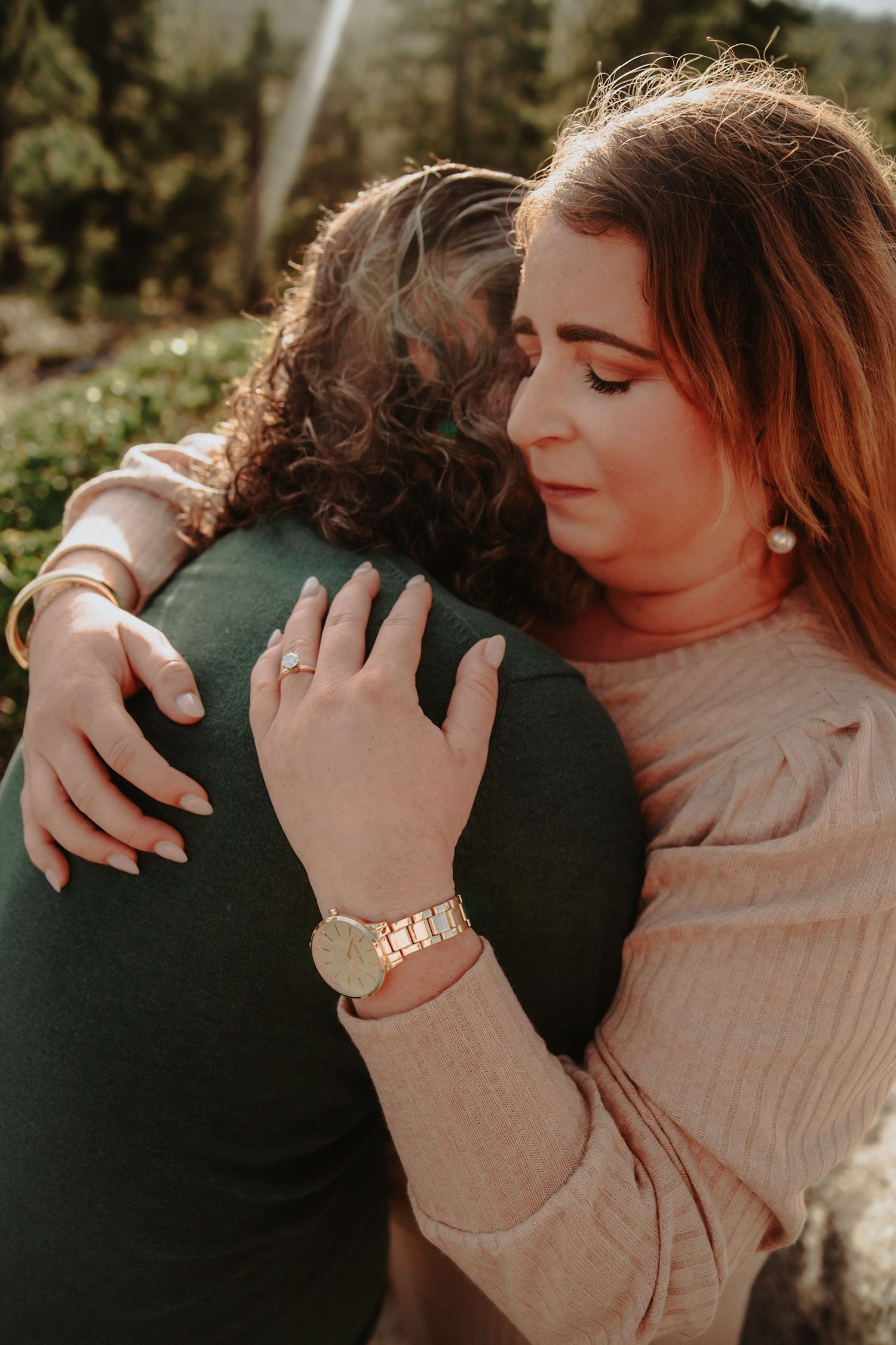 Woman hugging her partner showing an engagement ring and gold watch.