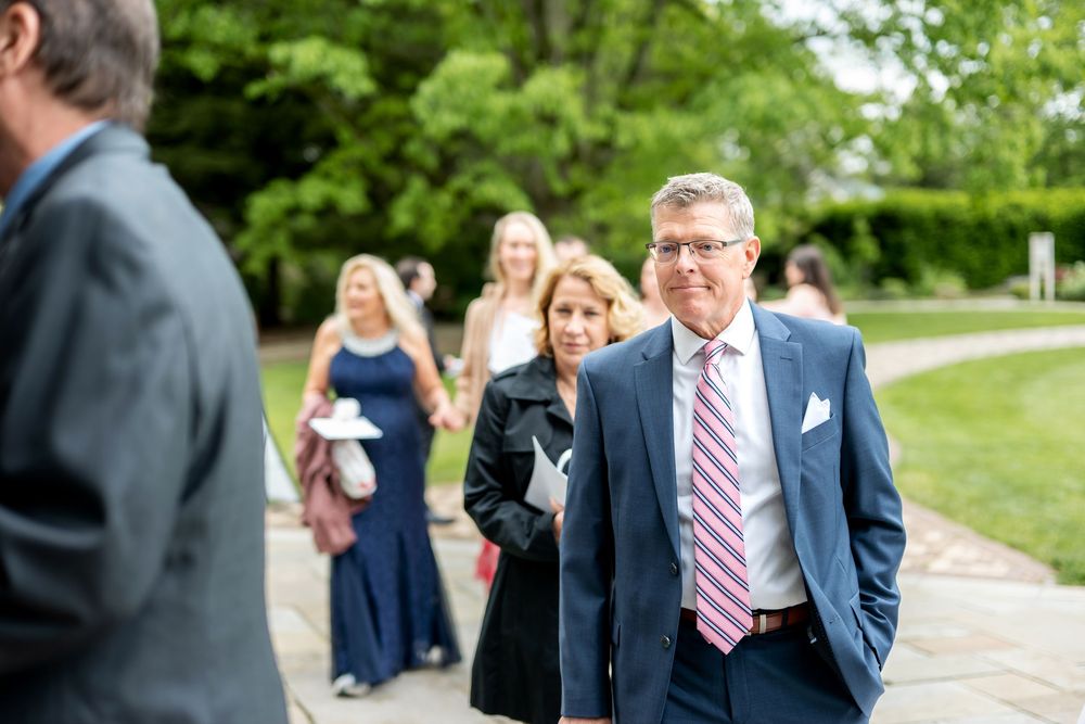Wedding guests in formal attire walking along outdoor pathway toward ceremony venue on sunny day.