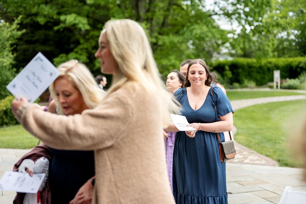 Wedding guests arrive outdoors, walking along a stone path surrounded by lush greenery.