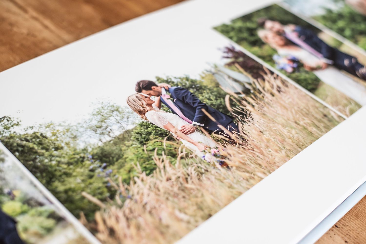 Open wedding photo album displaying romantic couple embracing in golden field, with lush green trees in background.