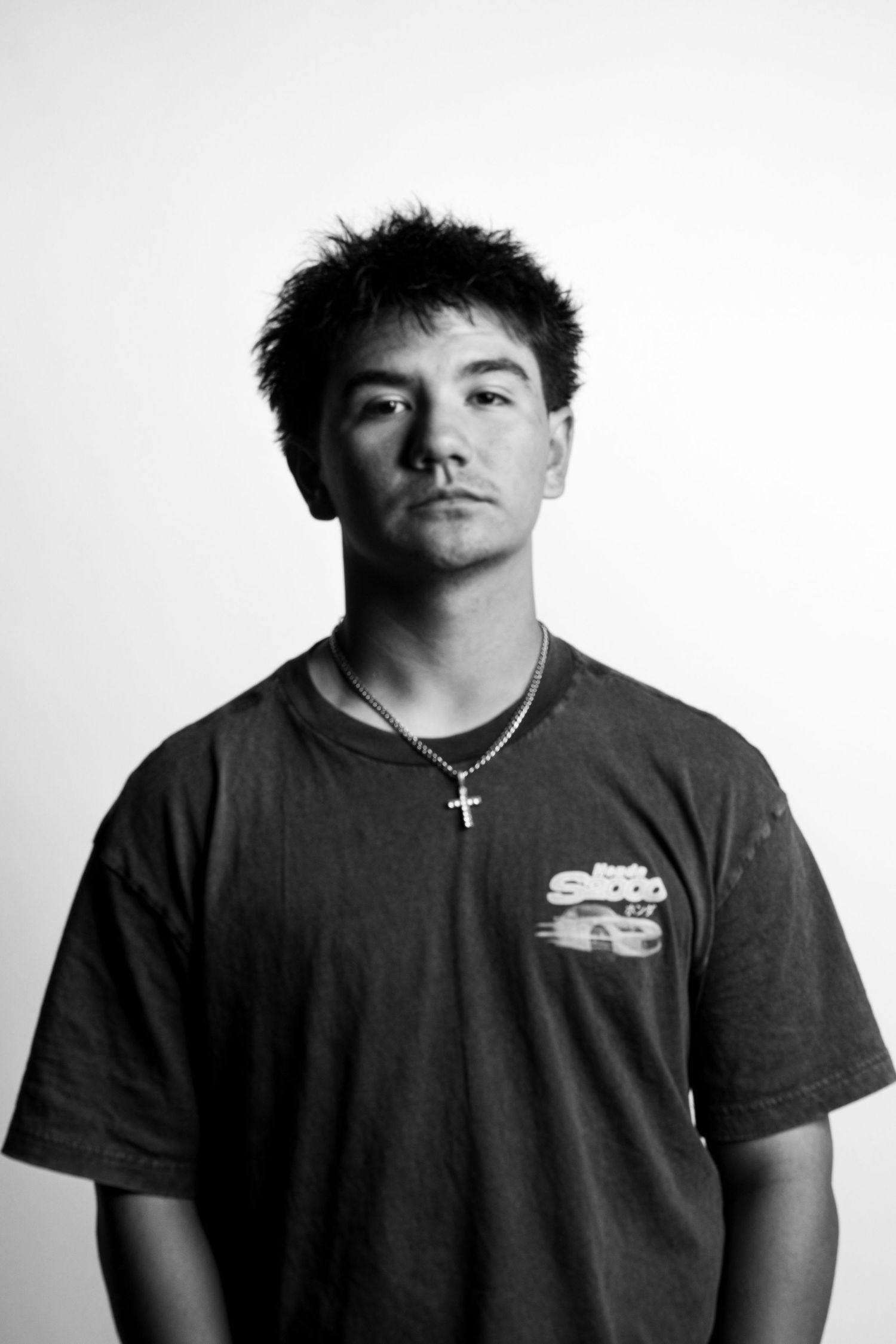 Black and white portrait of young man wearing cross necklace and dark graphic t-shirt.