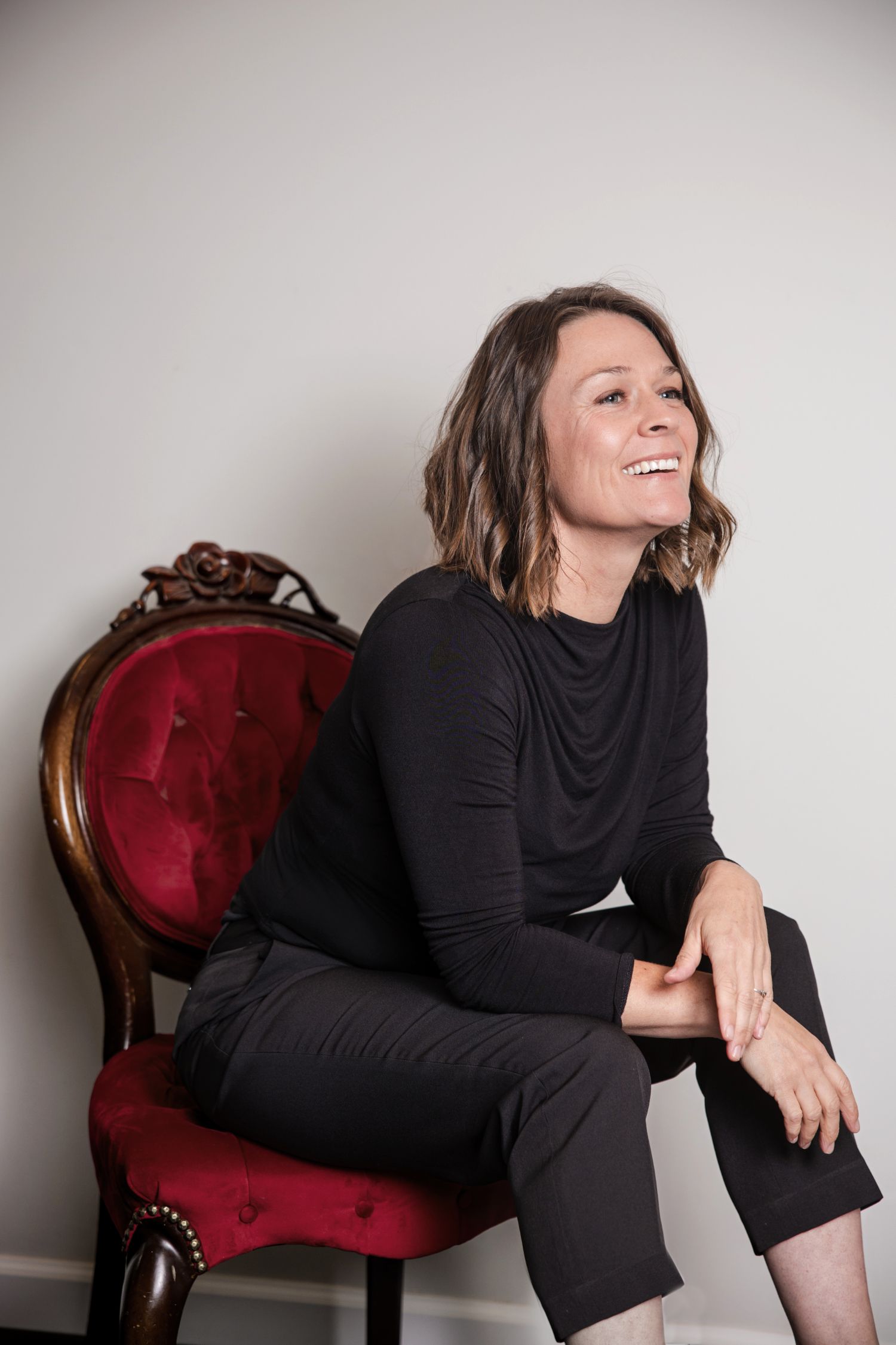 Professional portrait of a person in a white blouse with short wavy hair posing thoughtfully against a dark background.