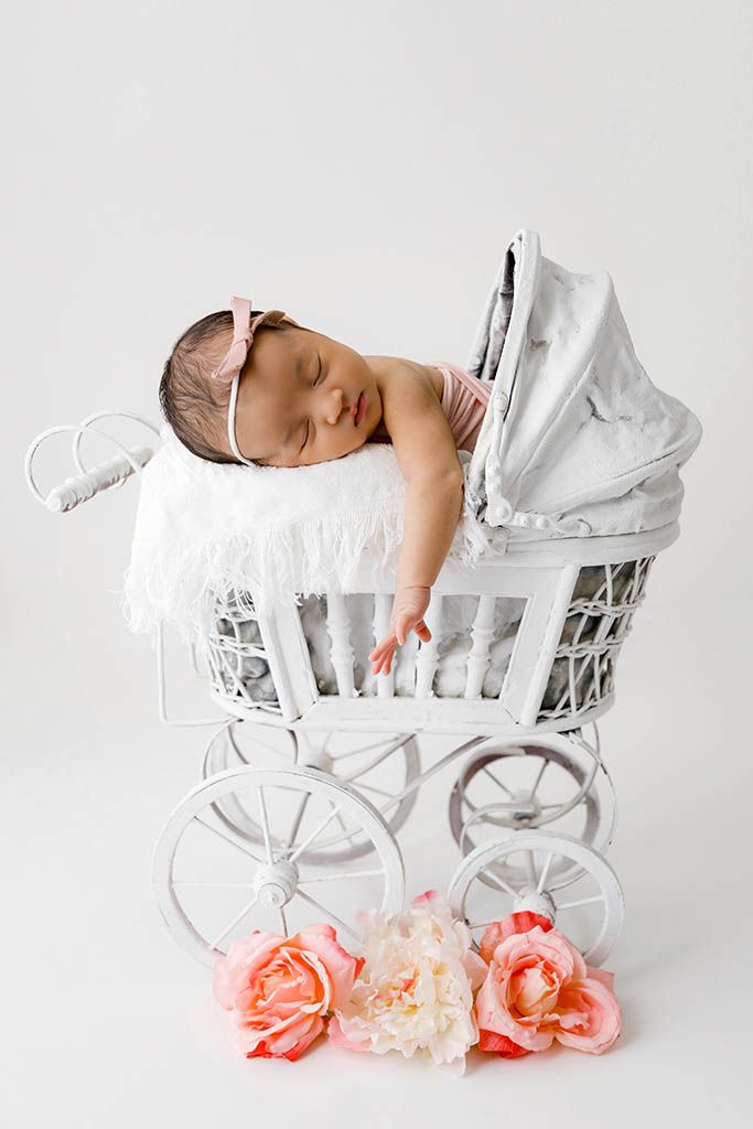 Peaceful newborn baby sleeping in a vintage white wicker pram with pink and white flowers.