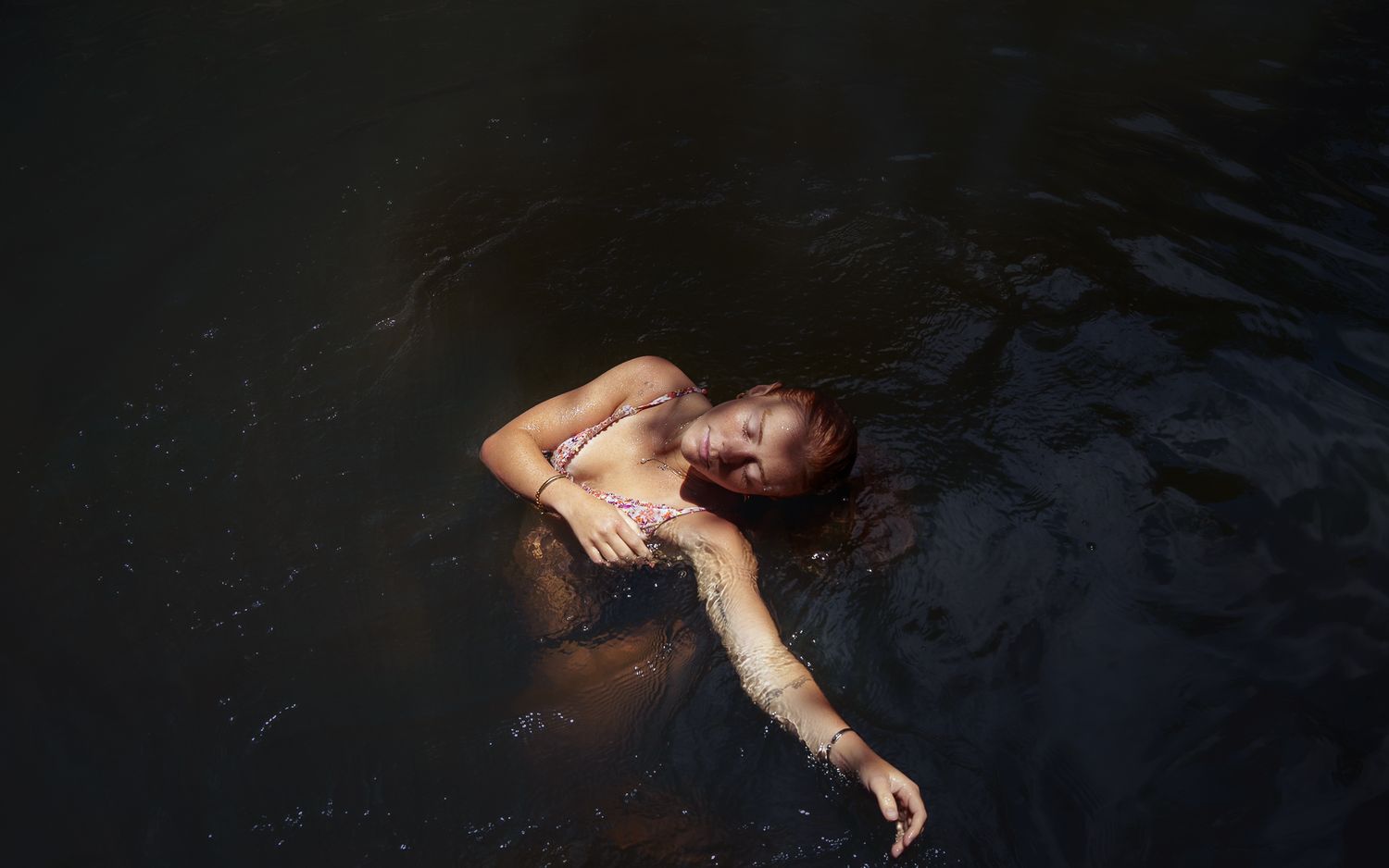 A young woman swimming in a waterfall in Hawaii.