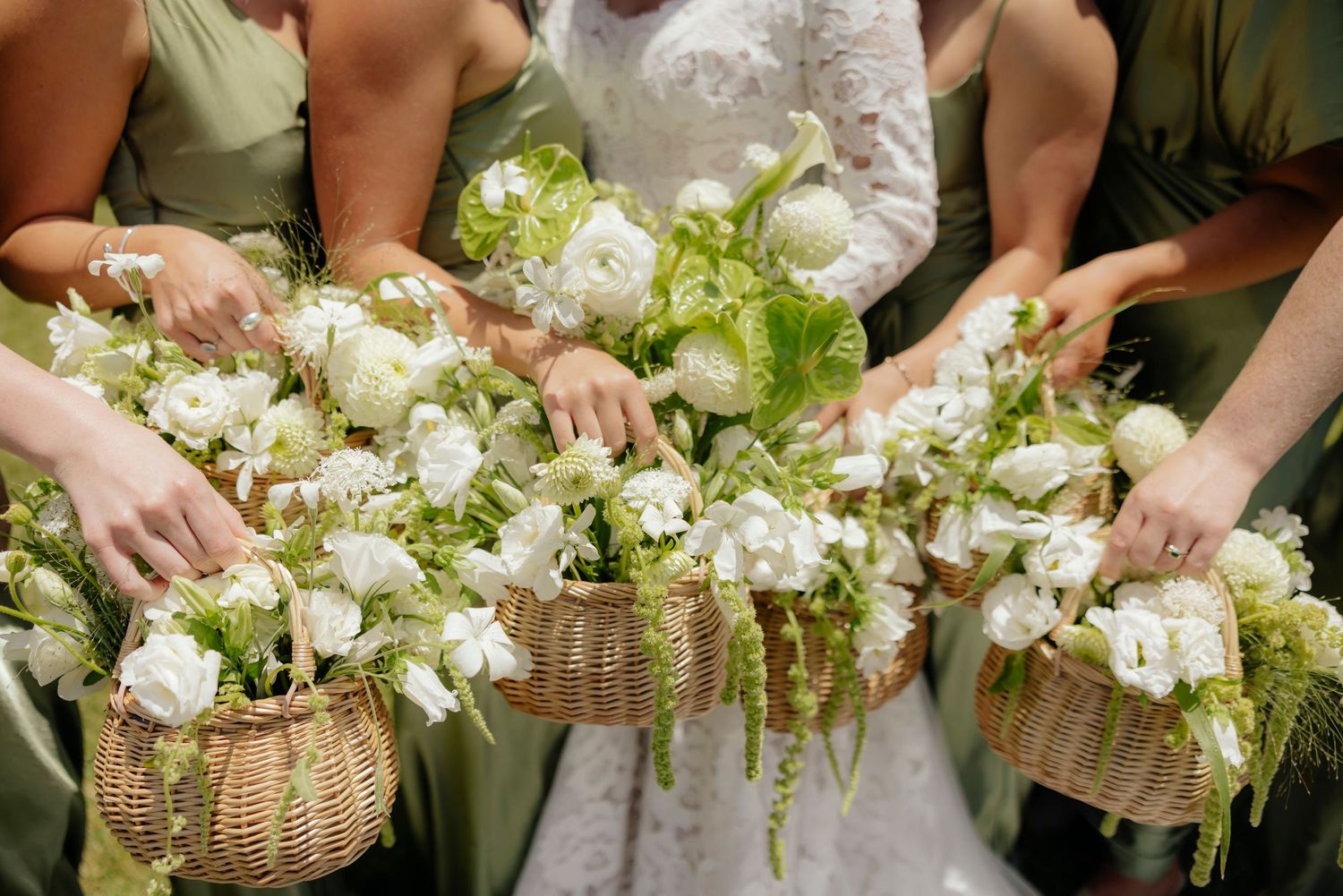 Bridesmaids holding rustic woven baskets filled with elegant white and green floral arrangements at a wedding ceremony.