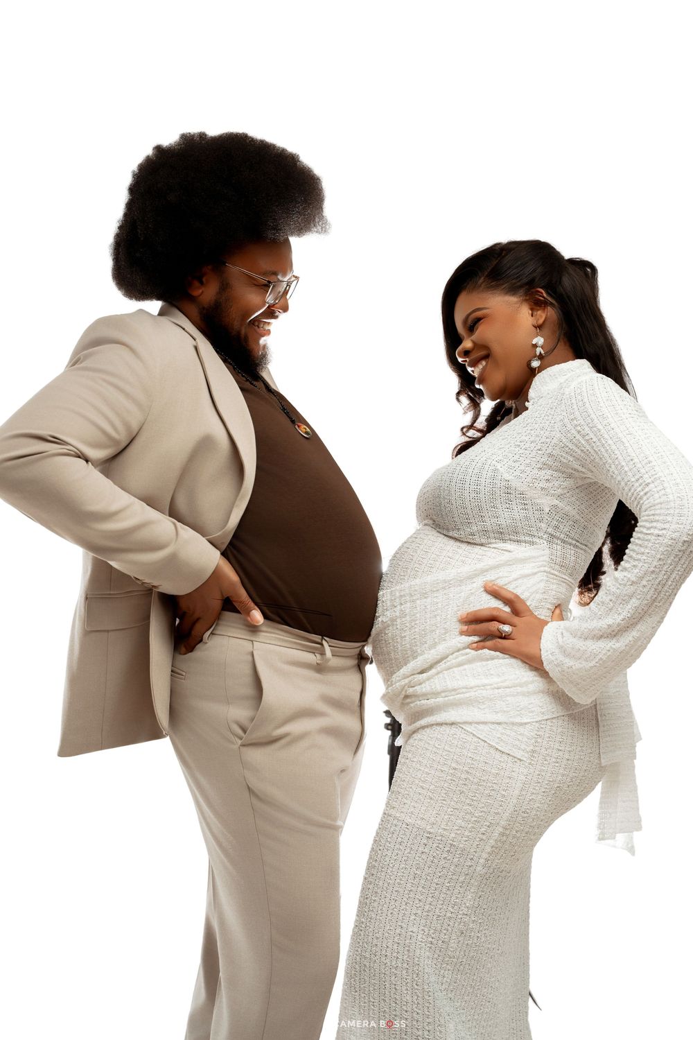 Couple laughing together at maternity photoshoot, man in beige suit and pregnant woman in white dress.