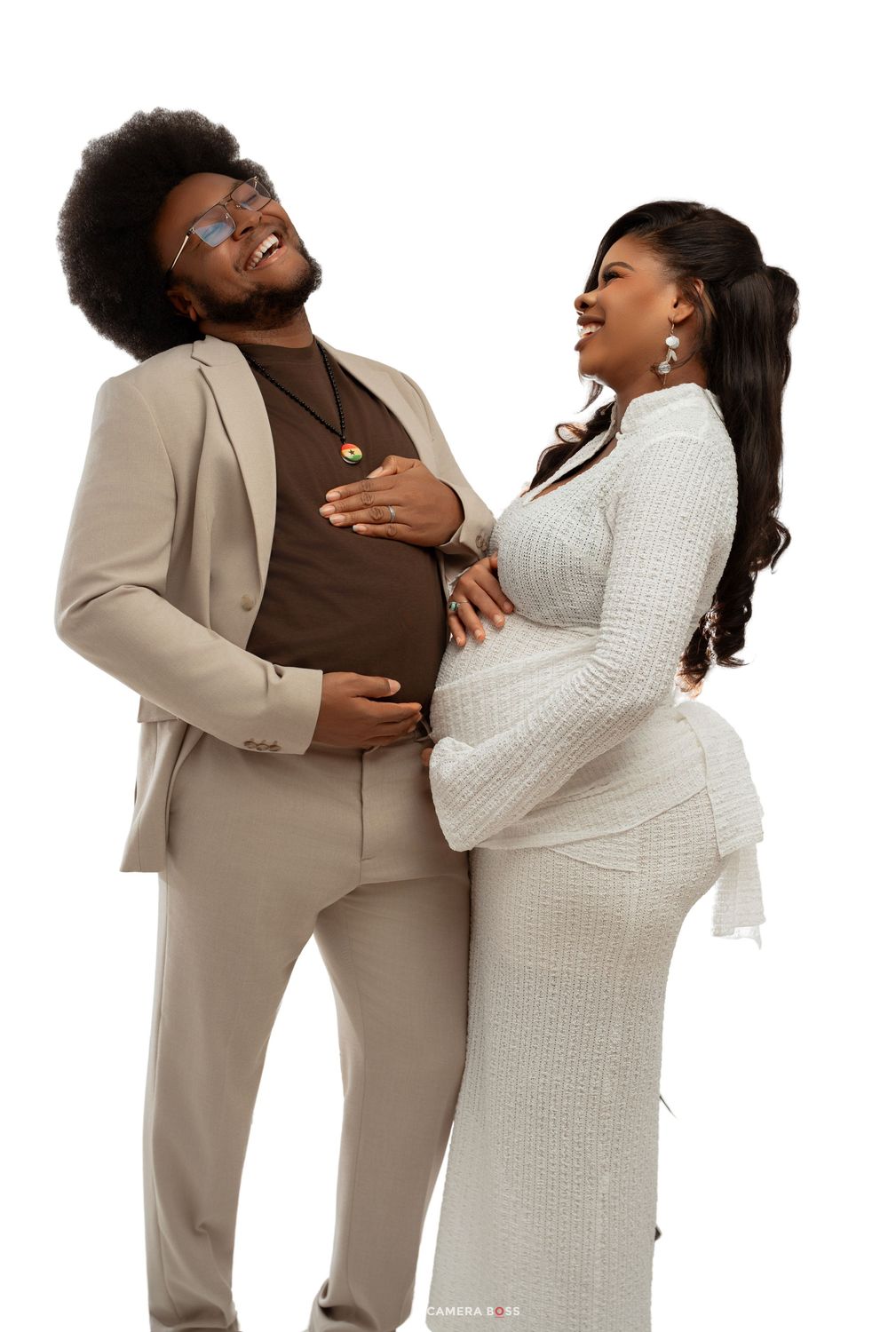 A joyful pregnant couple poses together, man in beige suit and woman in white dress, both smiling and cradling her baby bump.