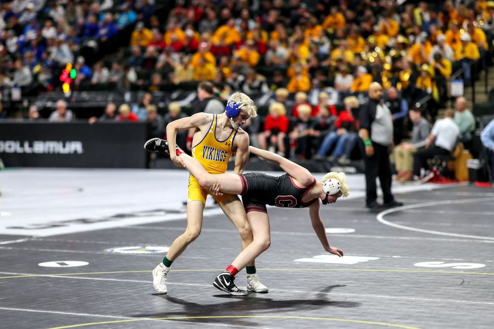 Two wrestlers compete on the mat during a high school wrestling tournament in a packed arena.