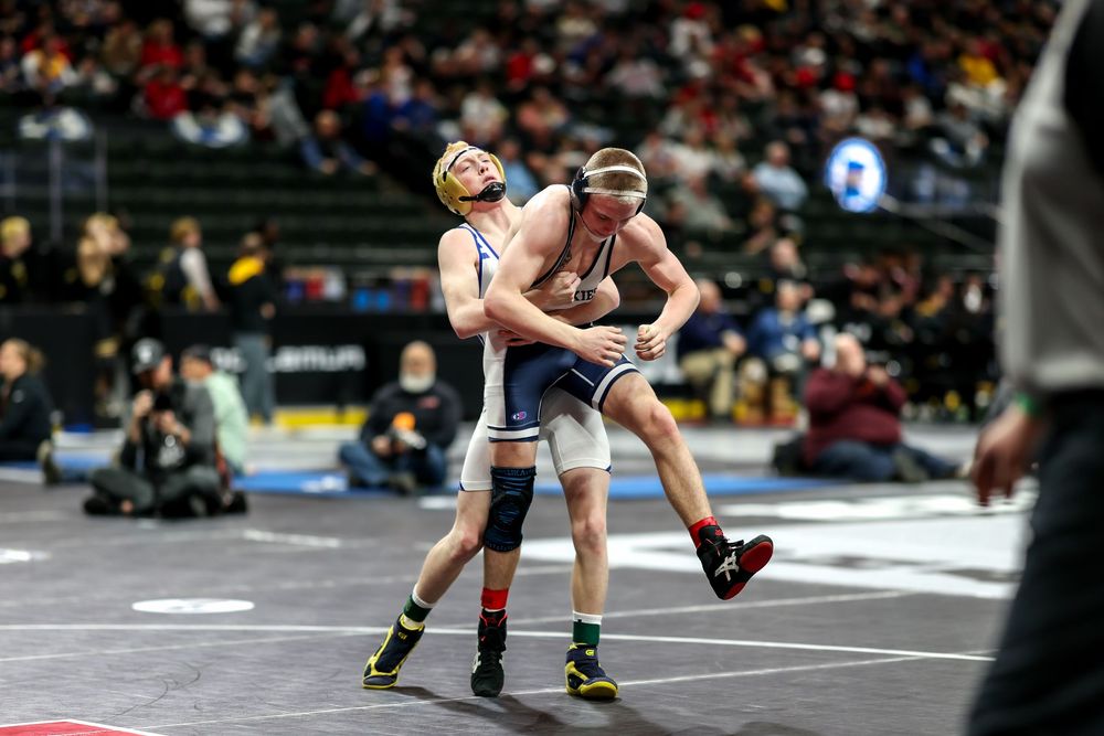 Two wrestlers compete in a high school wrestling tournament match on a mat inside a large arena.