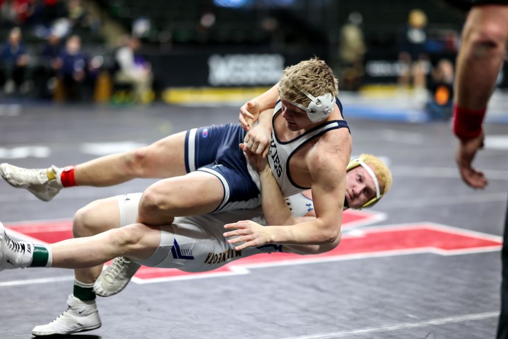 Two wrestlers compete on a mat, with one athlete in blue executing a takedown move during a wrestling tournament match.