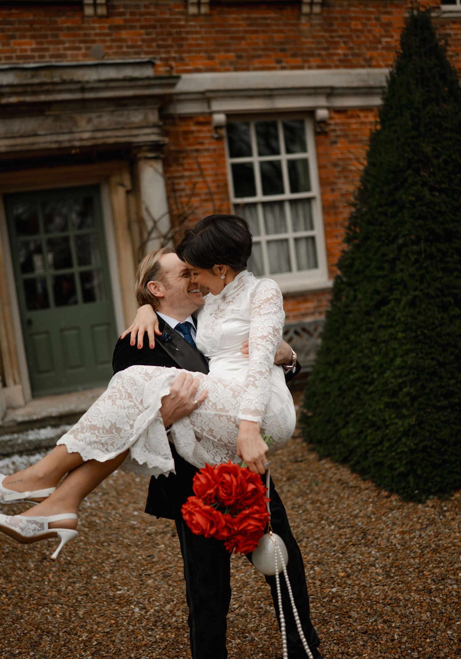 Emotional groom covering his face with hands during first look at bride holding red and white bouquet.