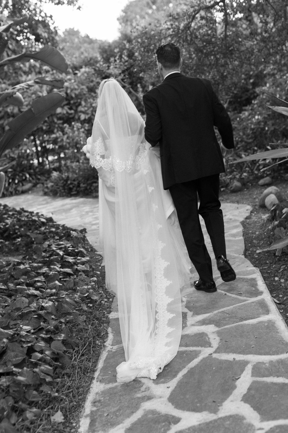 Classic black and white photo of bride and groom walking through gardens in Santa Barbara