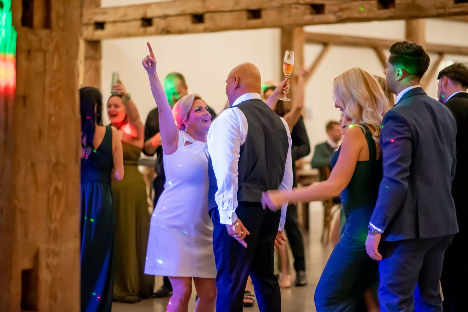 Bride and groom share a joyful dance with guests at lively wedding reception inside rustic barn venue.