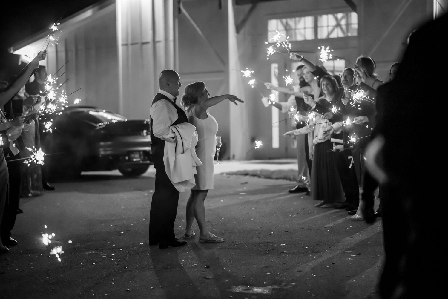 Black and white wedding sparkler exit photo of bride and groom walking through guests holding sparklers at night.