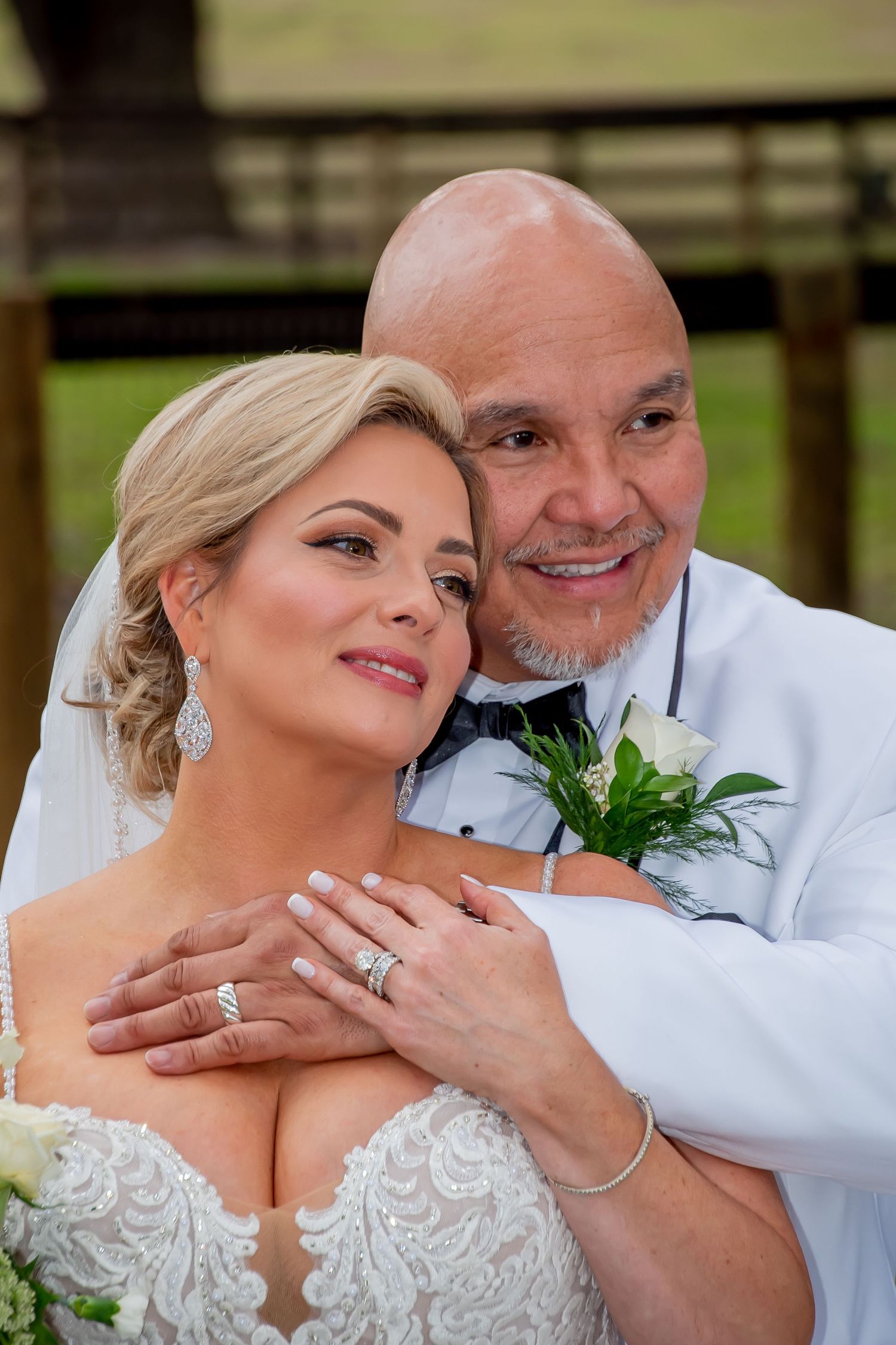 Newlywed couple poses closely together, bride in lace gown with bouquet and groom in white jacket.