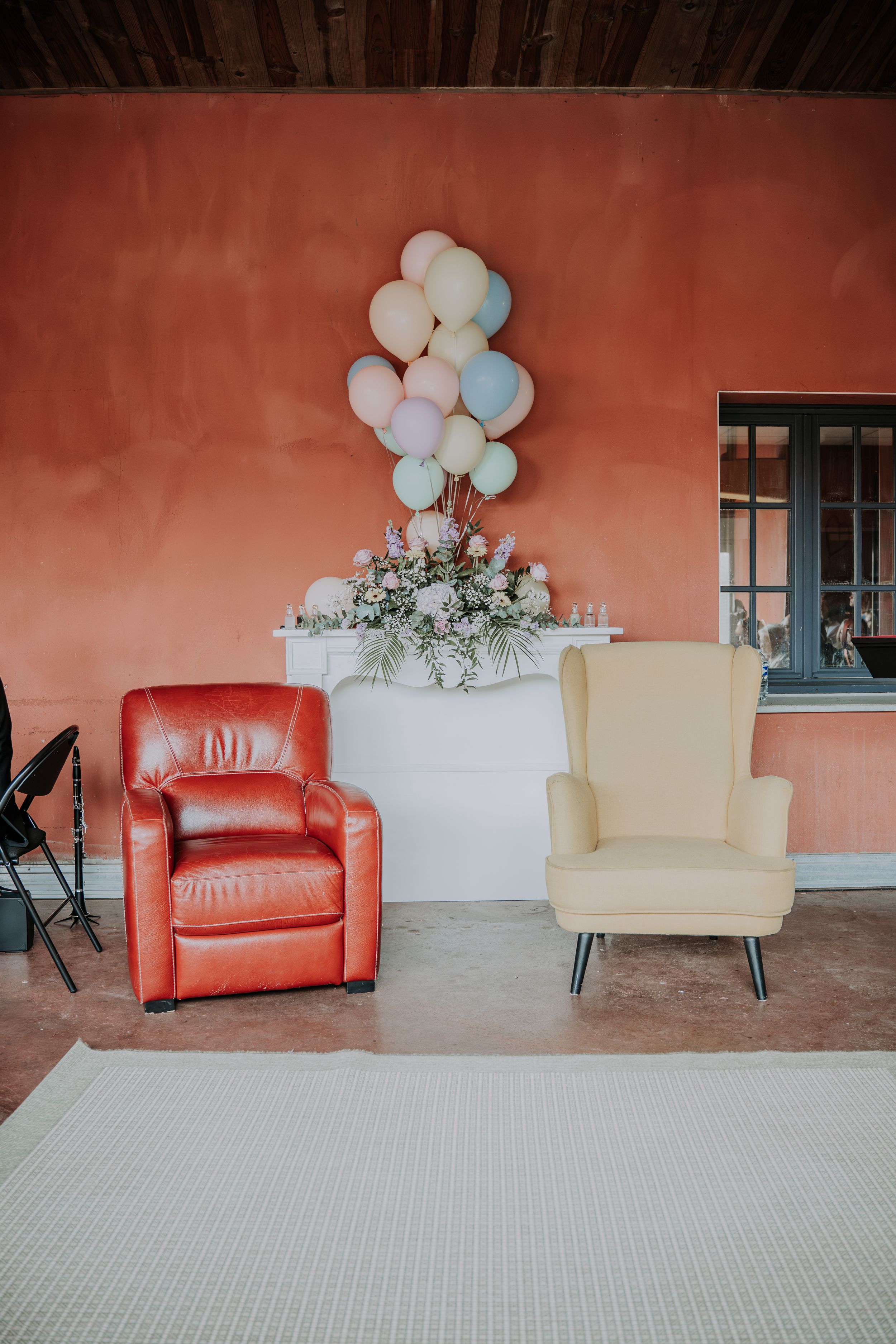Red leather and cream armchairs beside a white table with flowers and pastel balloons against a coral wall.