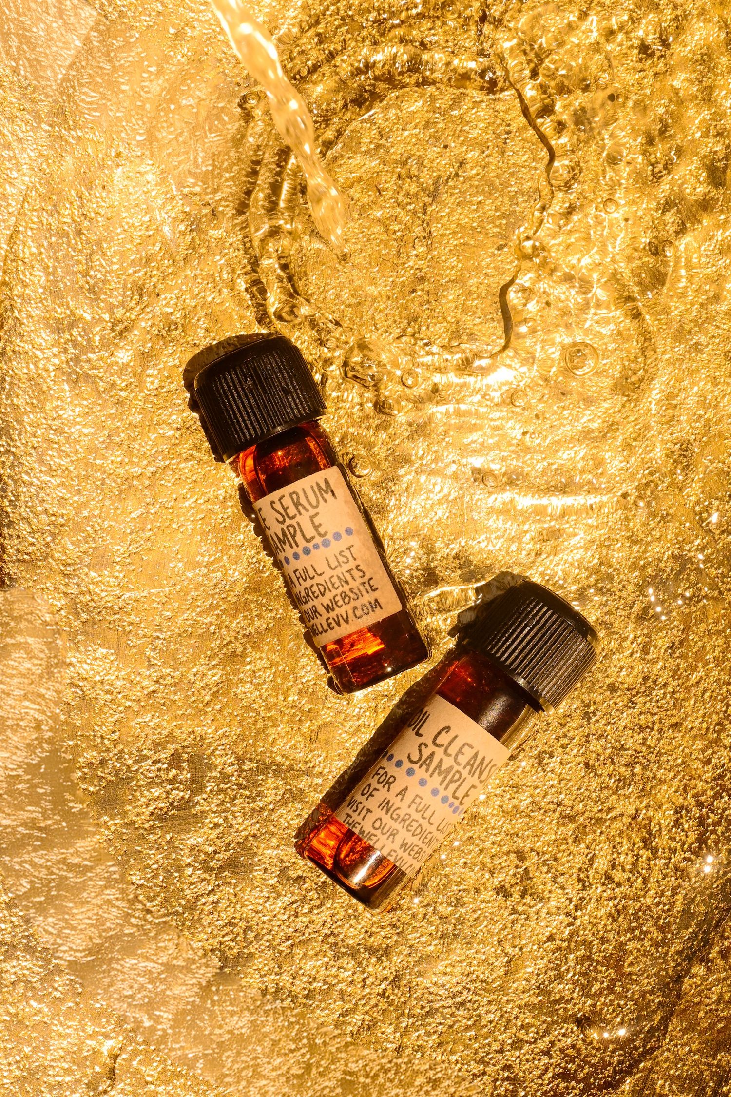 Two amber glass serum sample bottles with black caps resting on a shimmering gold wet surface.