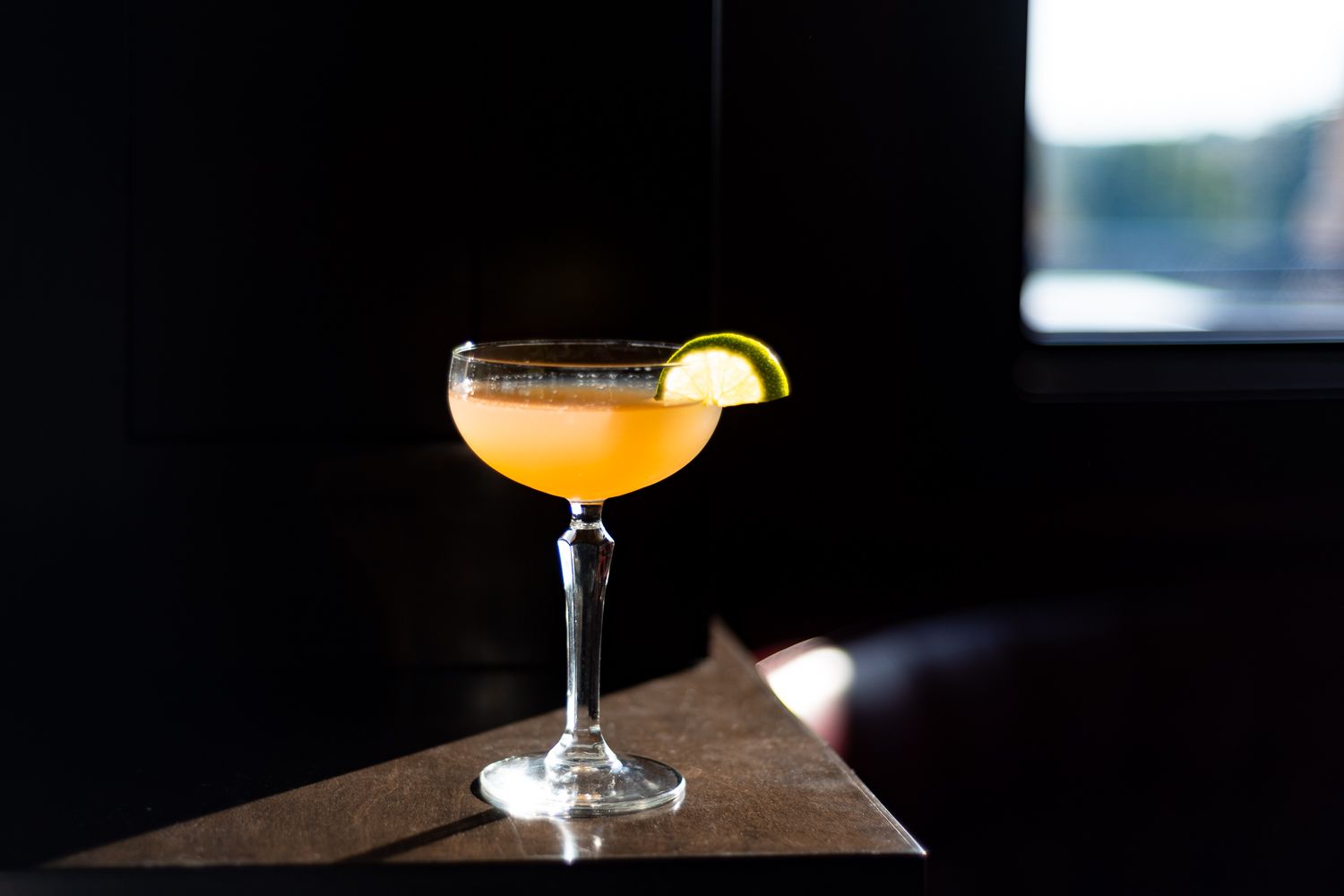 Craft cocktail in coupe glass garnished with citrus slice against dark background.