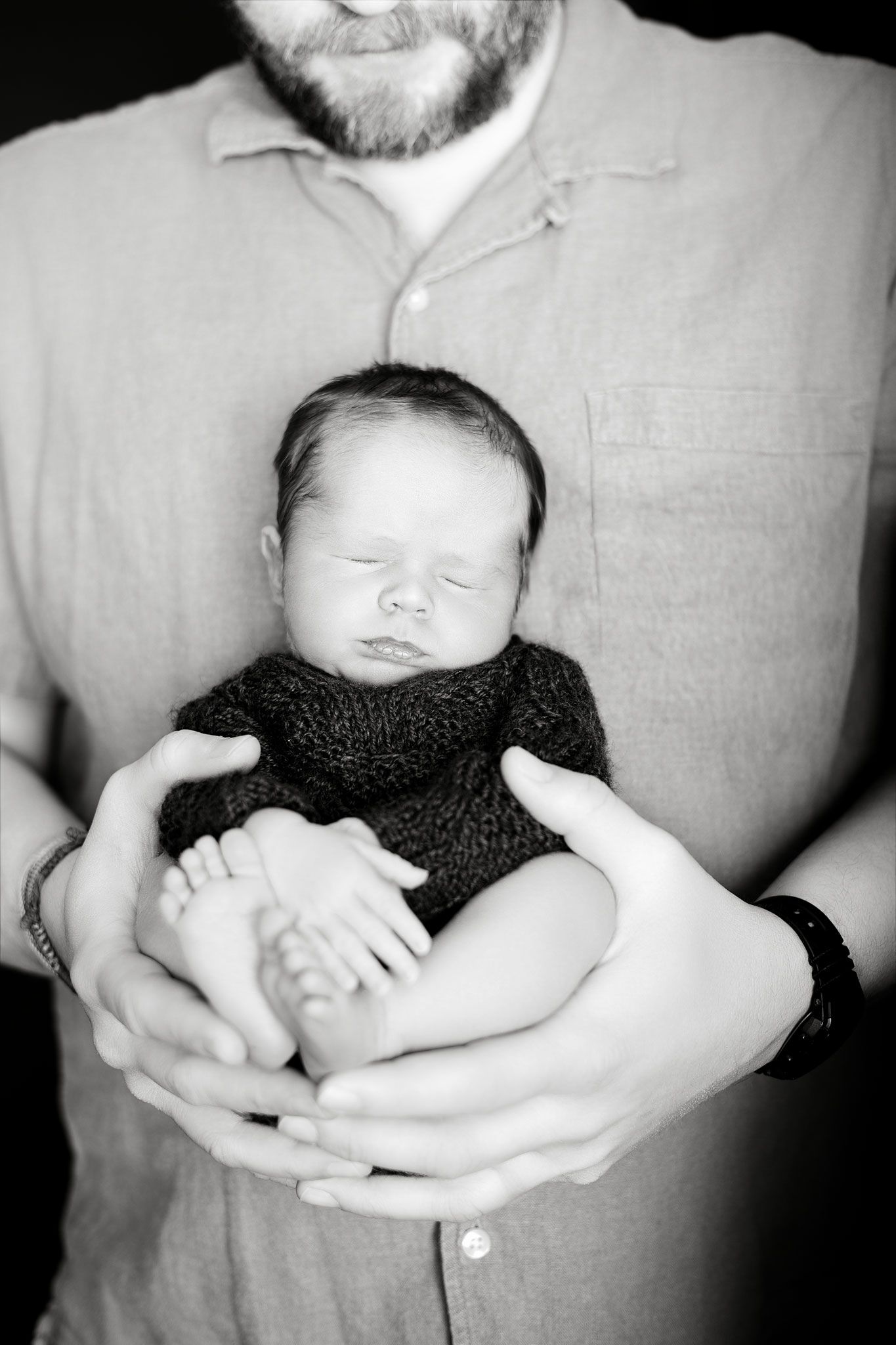 A peaceful black and white portrait of a sleeping newborn baby being cradled in gentle arms.