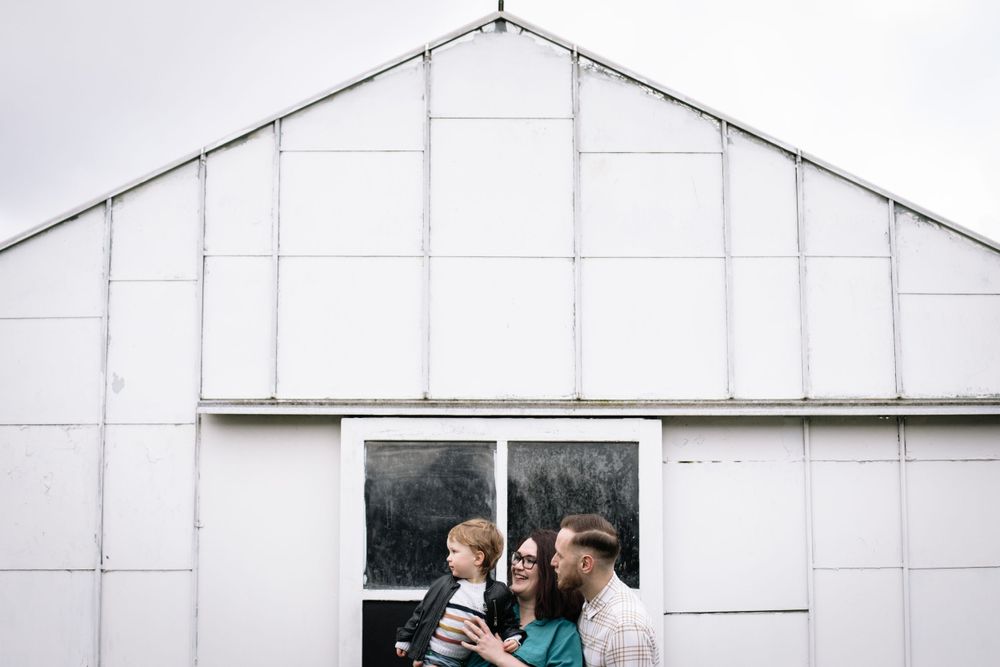 Three figures stand together in front of a white barn-like structure with dark windows.